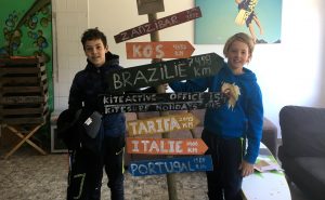twee jonge kitesurfers staan met wegbewijzering naar tropische kitesurf oorden